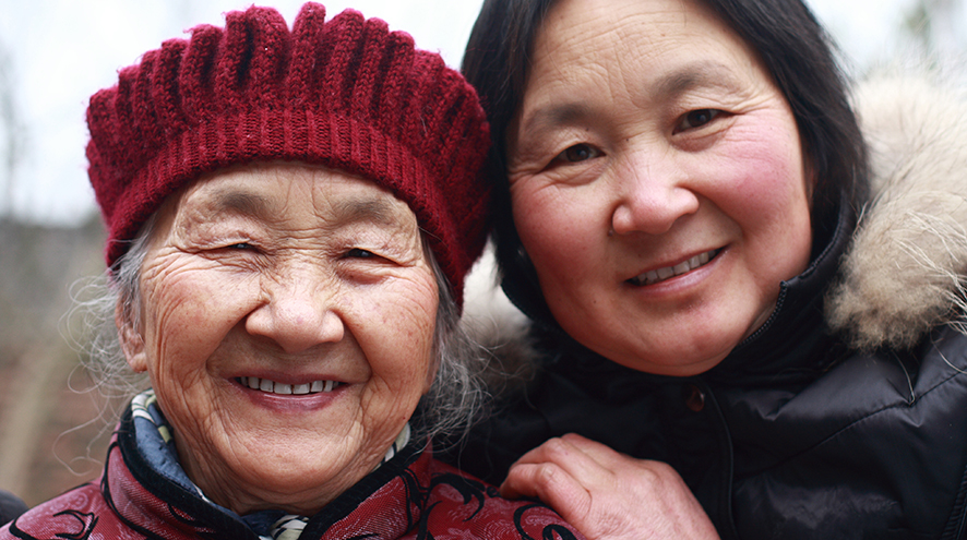 Mother and daughter standing and smiling at the camera, wearing winter clothing.